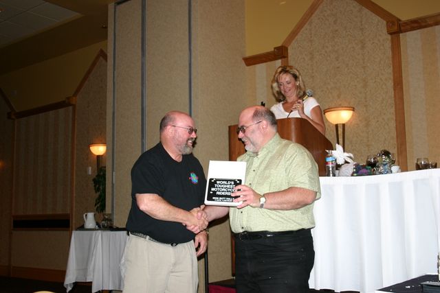 Two riders shake hands as an Iron Butt Rally finisher's plaque reading "World's Toughest Motorcycle Riders" is presented at the 2005 finishers' banquet.