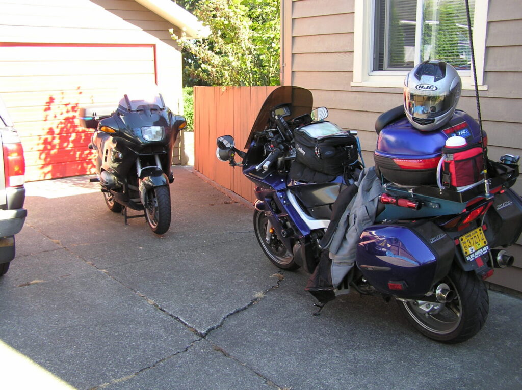 A blue 2005 Yamaha FJR1300 loaded for a long ride, with a helmet on the top box, a hydration bag, a CB antenna and a flat platform under the top box.